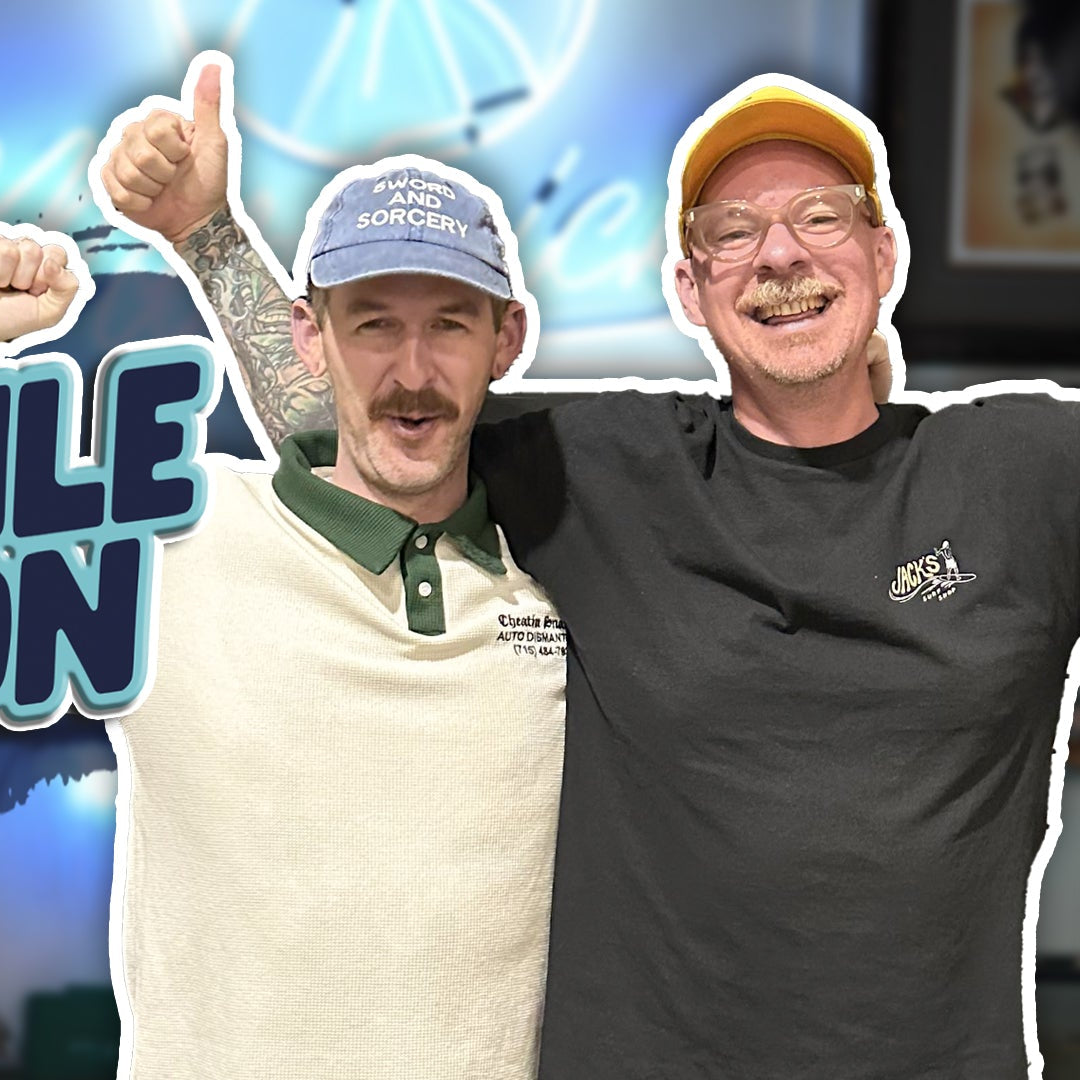 Two men posing with a cutout sign for 'Crocodile Jackson' in a tattoo supply store.